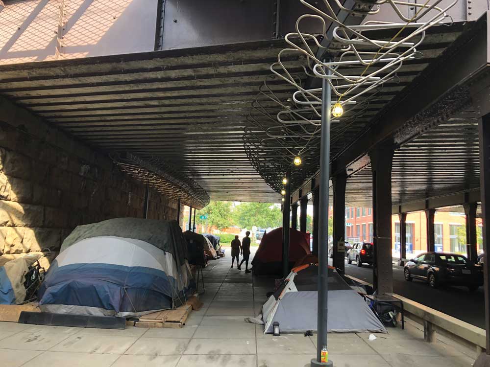 tents on a broad sidewalk with an LED light installation above them