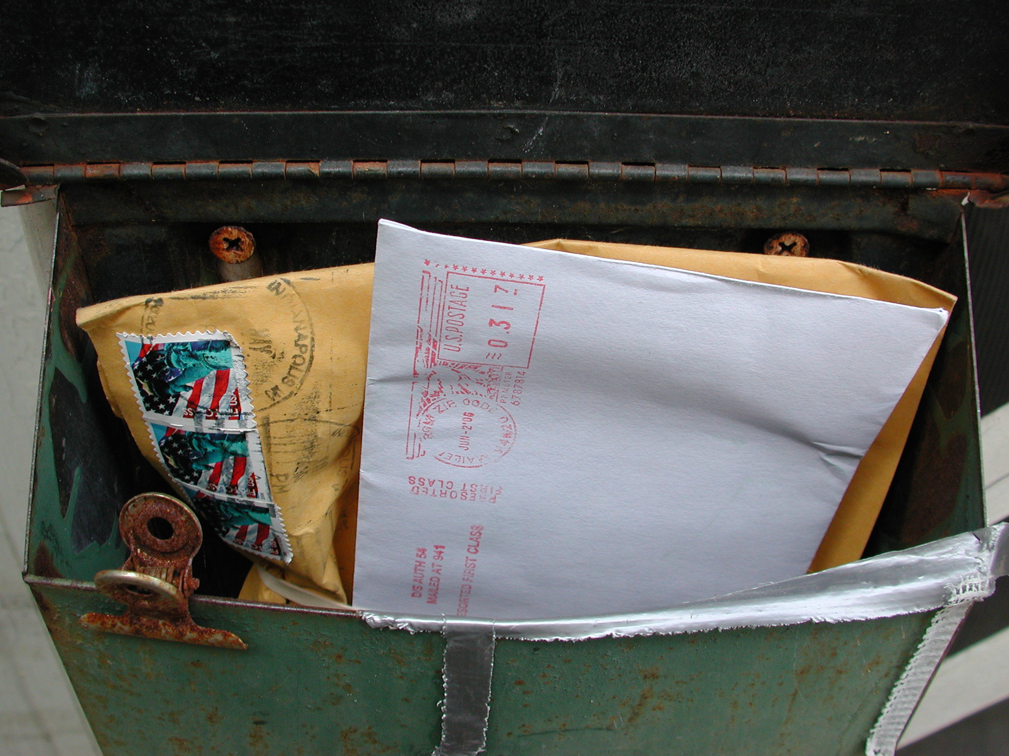 A green mailbox is stuffed with packages and letters.