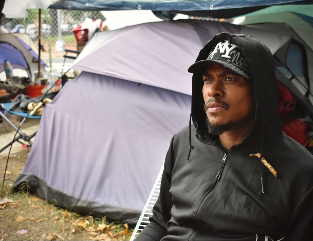 David, a homeless resident sits on a bench in the encampment while staring at the fencing around the park