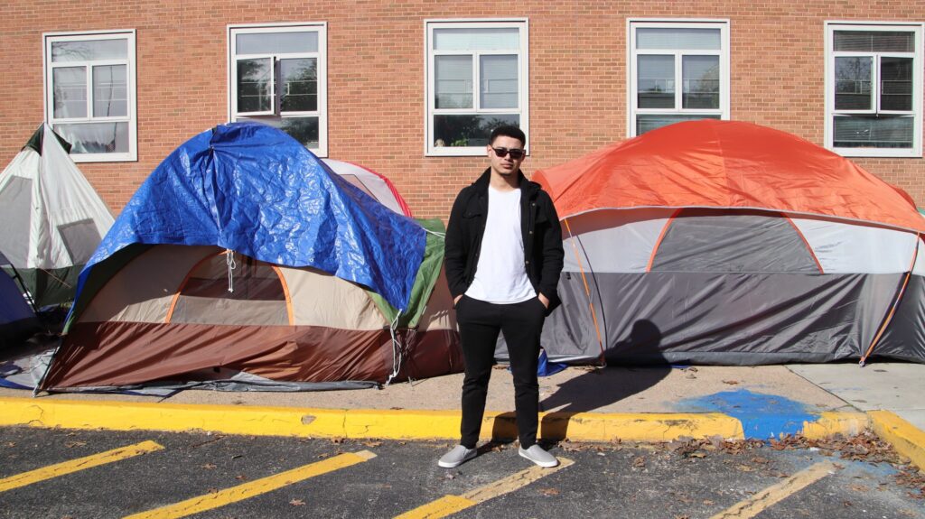 A young man stands in front of two tents on the side of the street.