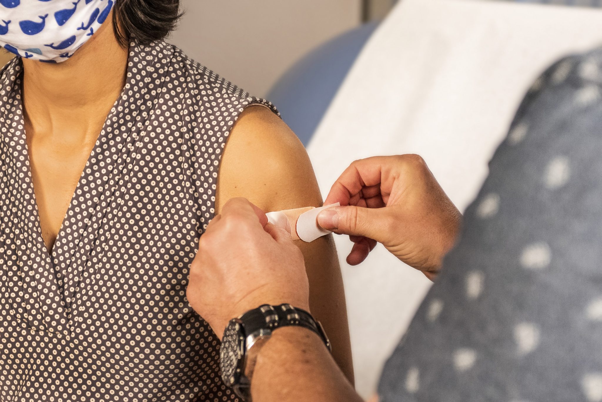 Photo of a woman wearing a mask having a band aid placed on her shoulder after getting a vaccine.