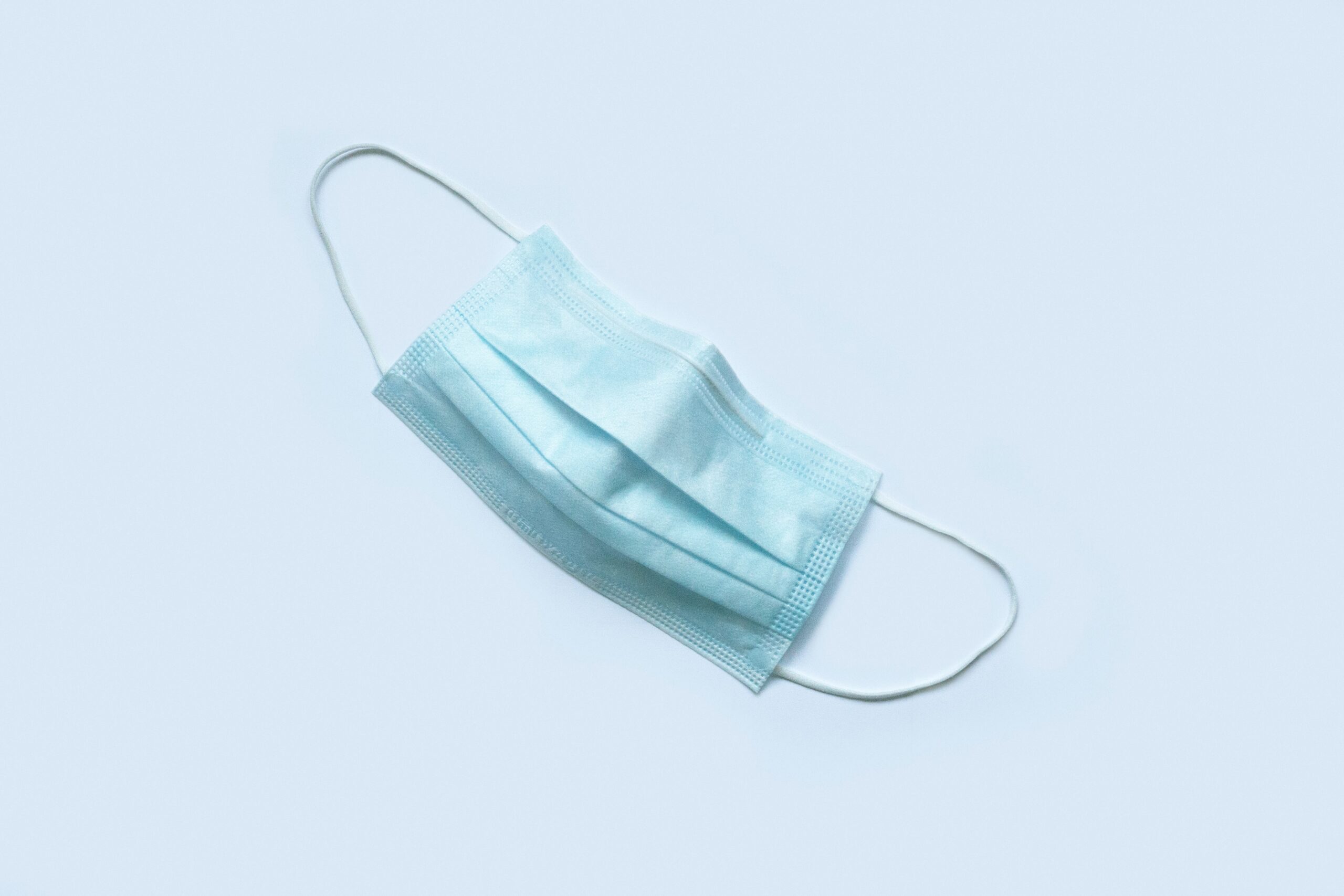 Photo of a blue surgical mask against a baby blue background.