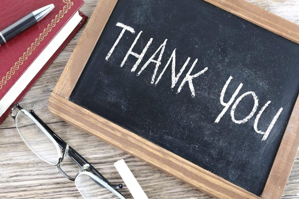 A picture of a chalk board with the phrase "Thank you" written in chalk. The chalk board is on a table along with a pair of glasses and pens.