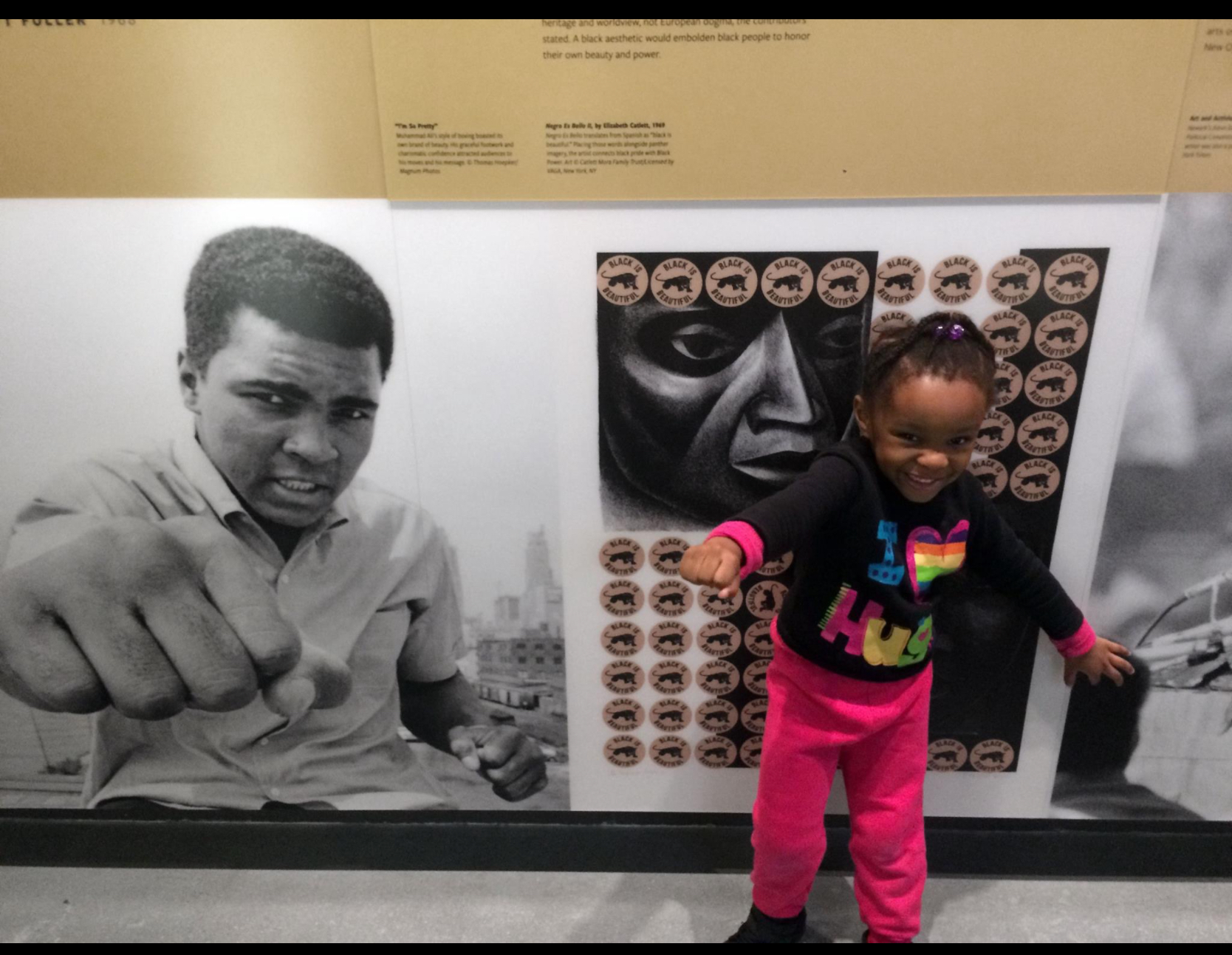 Photo of Muhammad Ali to the left with a young girl wearing pink pants and a black shirt imitating the photo to her right.