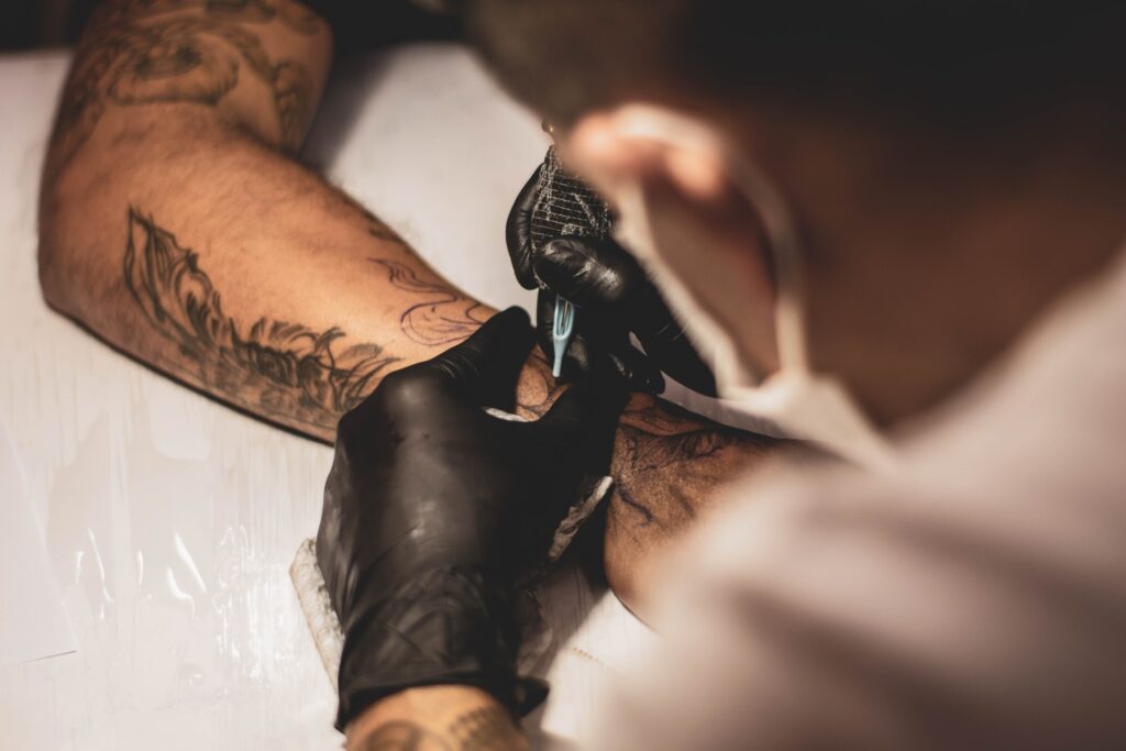 Photo of a tattoo artist, wearing black gloves, tattooing onto someone's forearm.