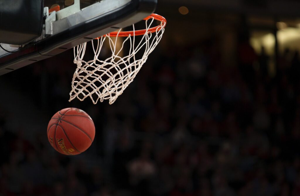 Photo of a basket ball going though a basket ball hoop.