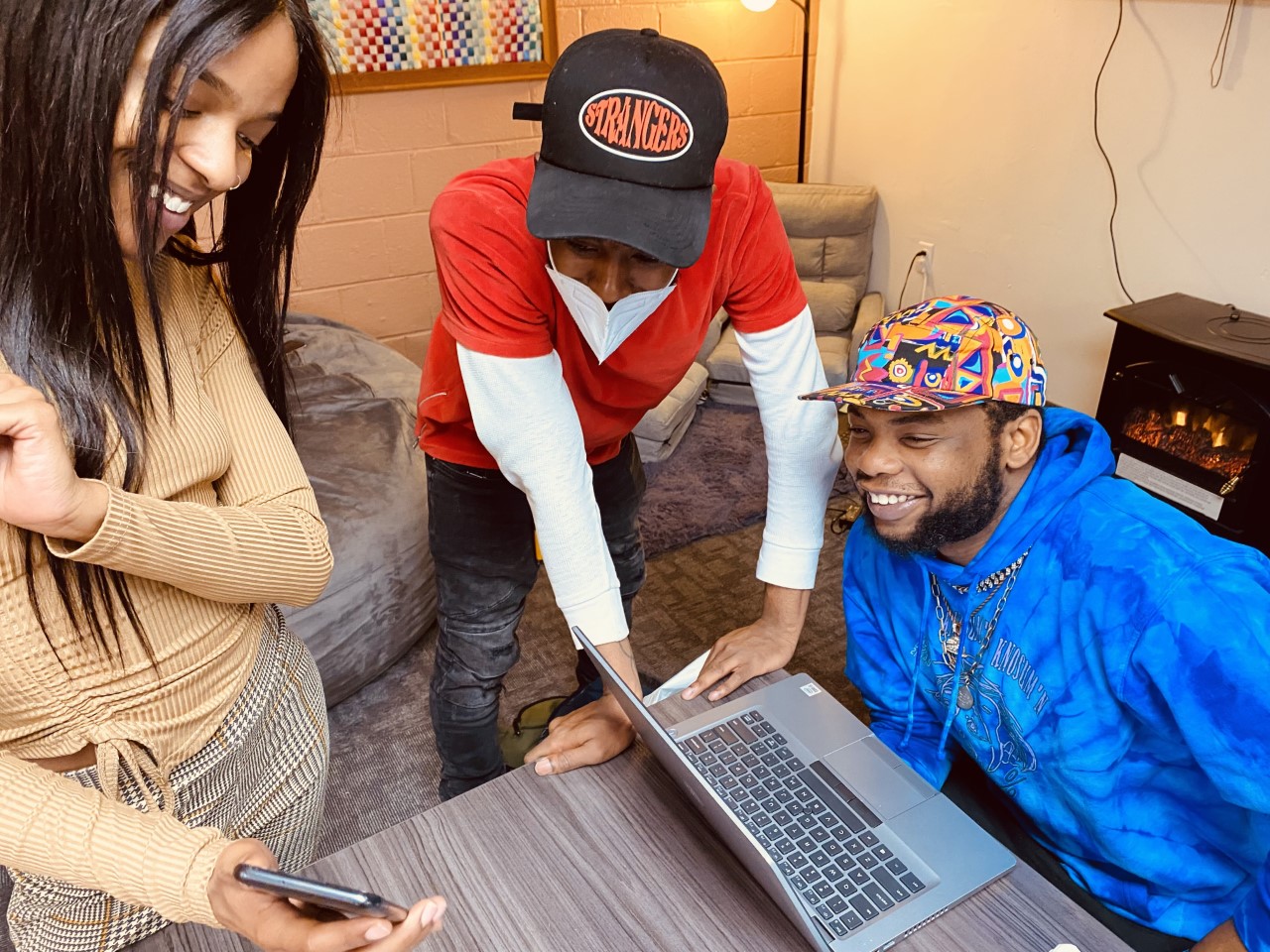 Three young people look at a phone and laptop.