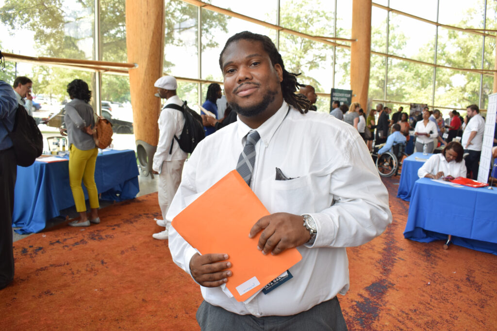 A Black man in a suit holds an orange folder.