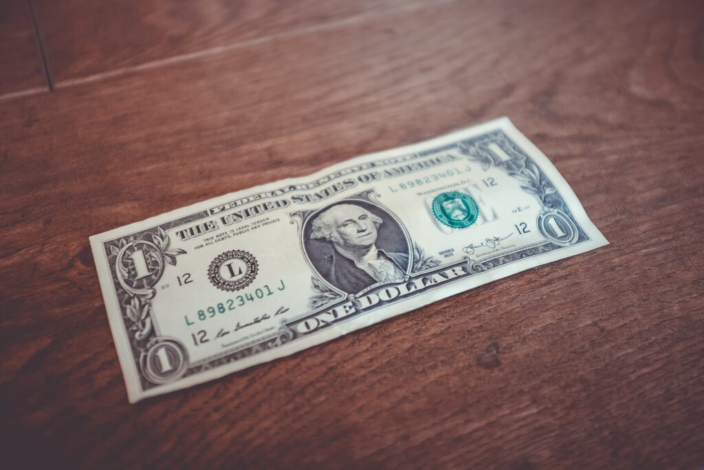 Photo of a $1 bill on a wood surface.