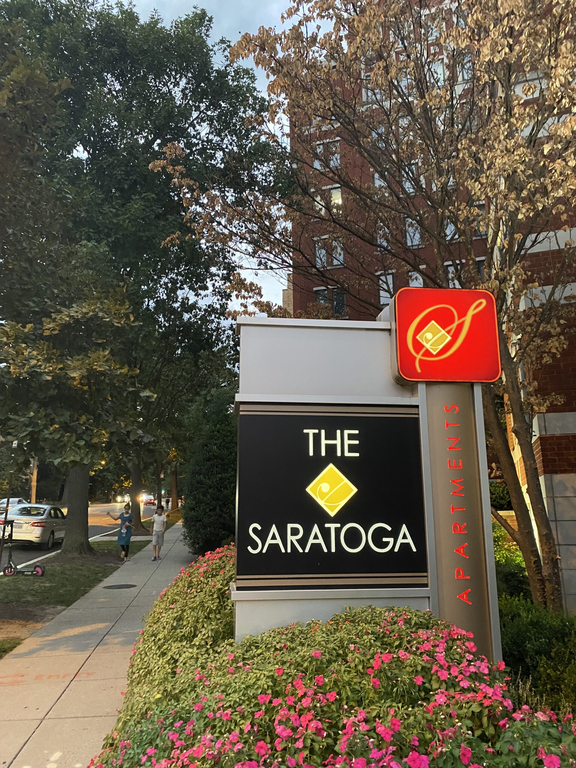 A black sign reading the Saratoga in front of an apartment building.
