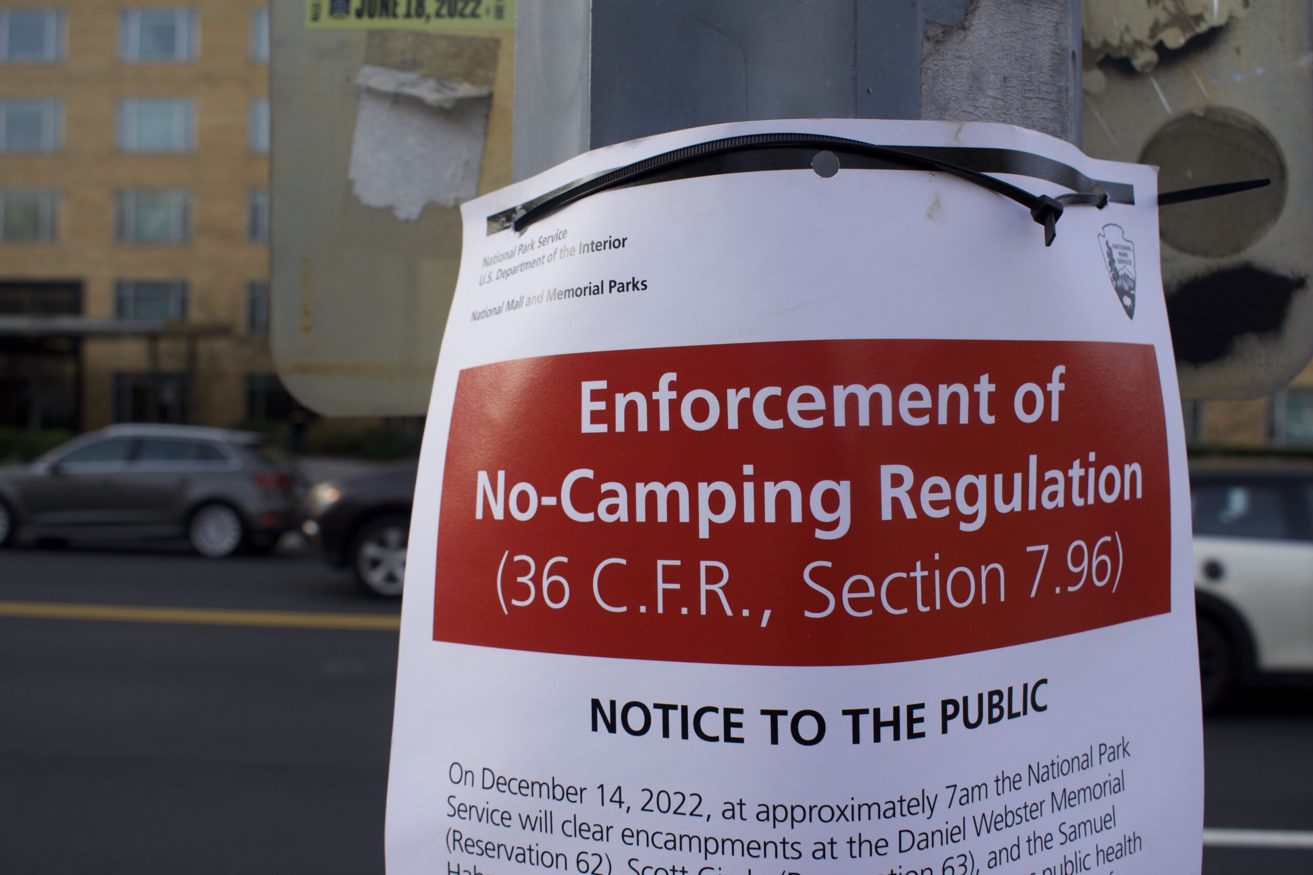 A sign taped to a pole notifies residents of a no-camping regulation.