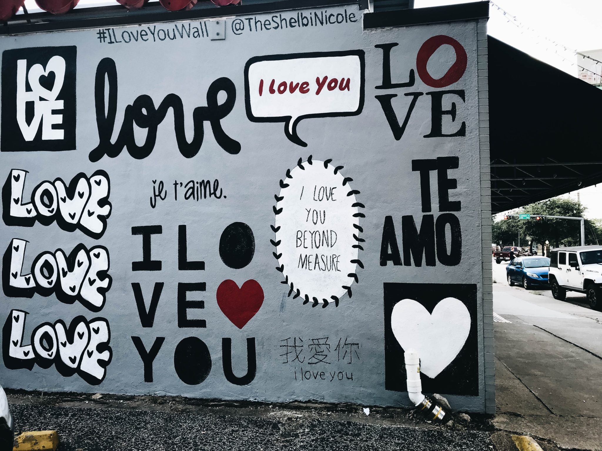 Photo of a grey wall painted with the message, "love" in different fonts and languages.