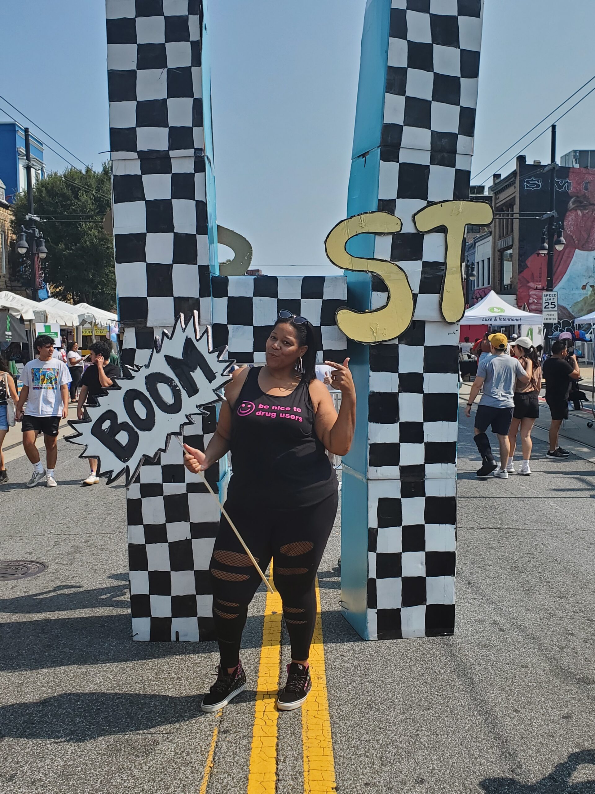 A woman poses in all black holding a sign that says "Boom."