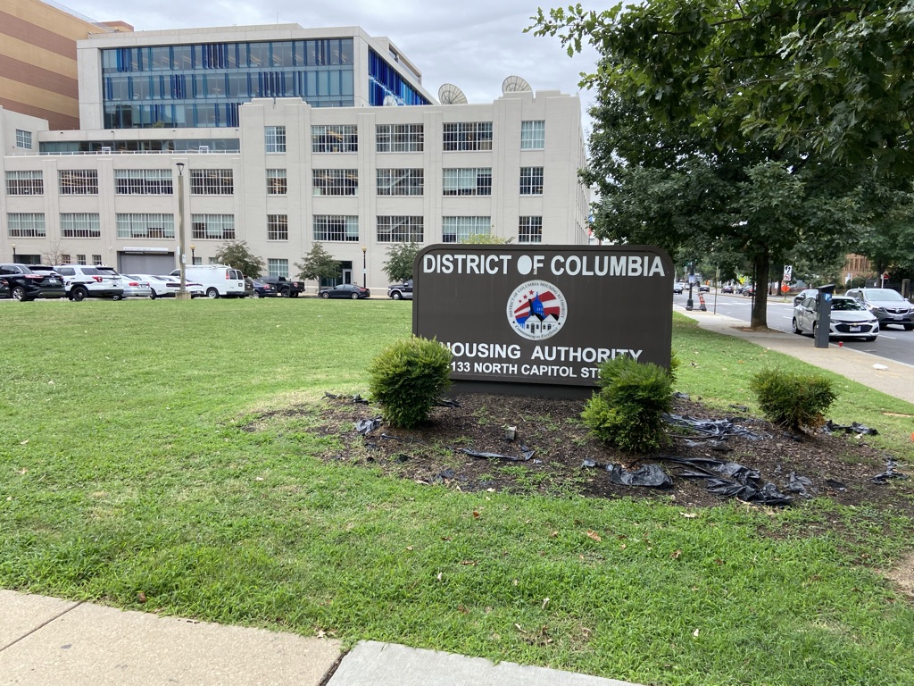 A sign reading "District of Columbia Housing Authority" in front of a white building.
