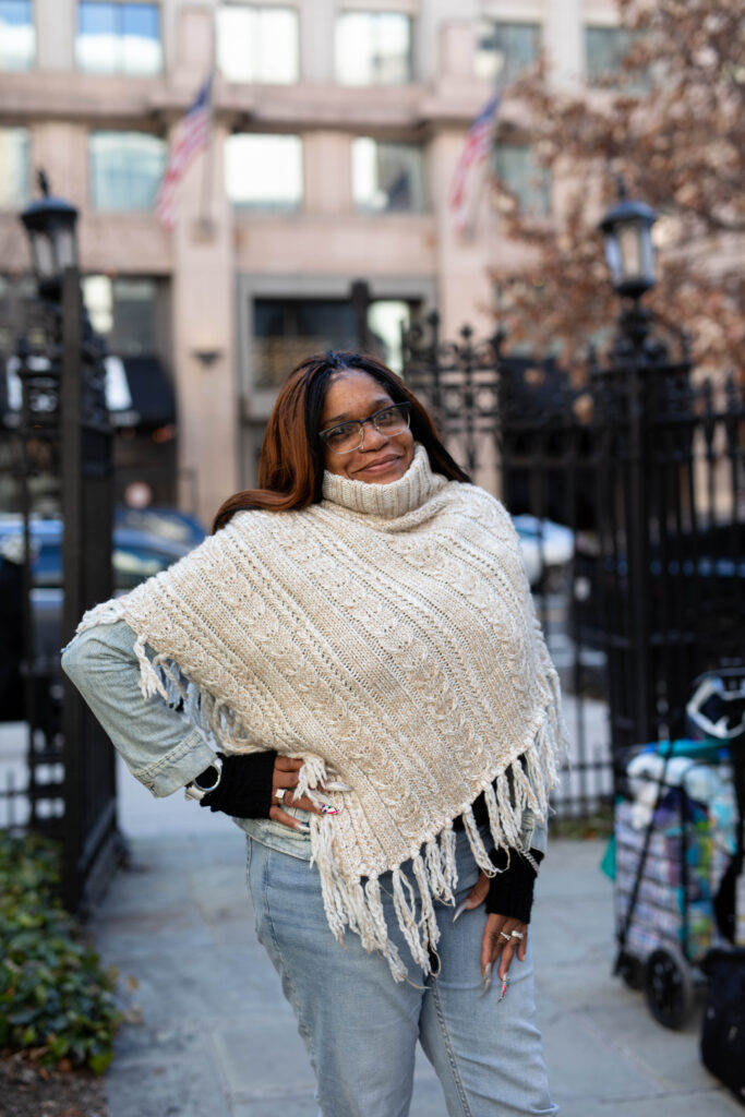 A Black woman poses, smiling, in front of black gates.