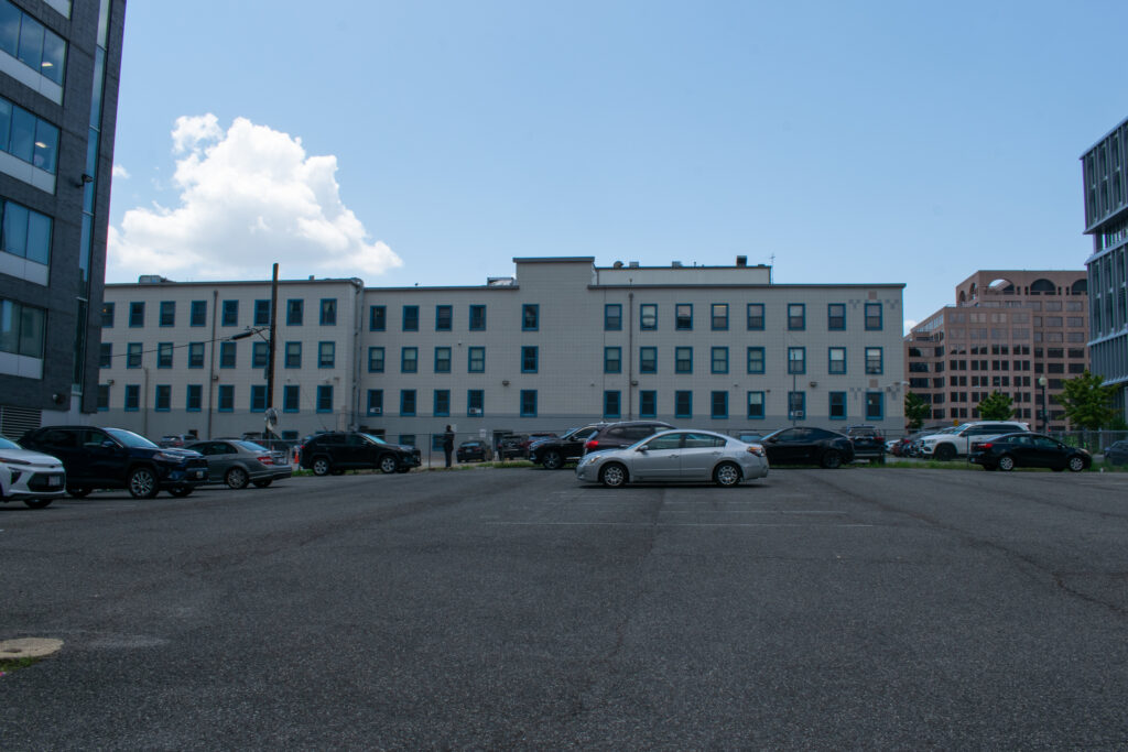 Across a grey parking lot, a long white building with blue windows.