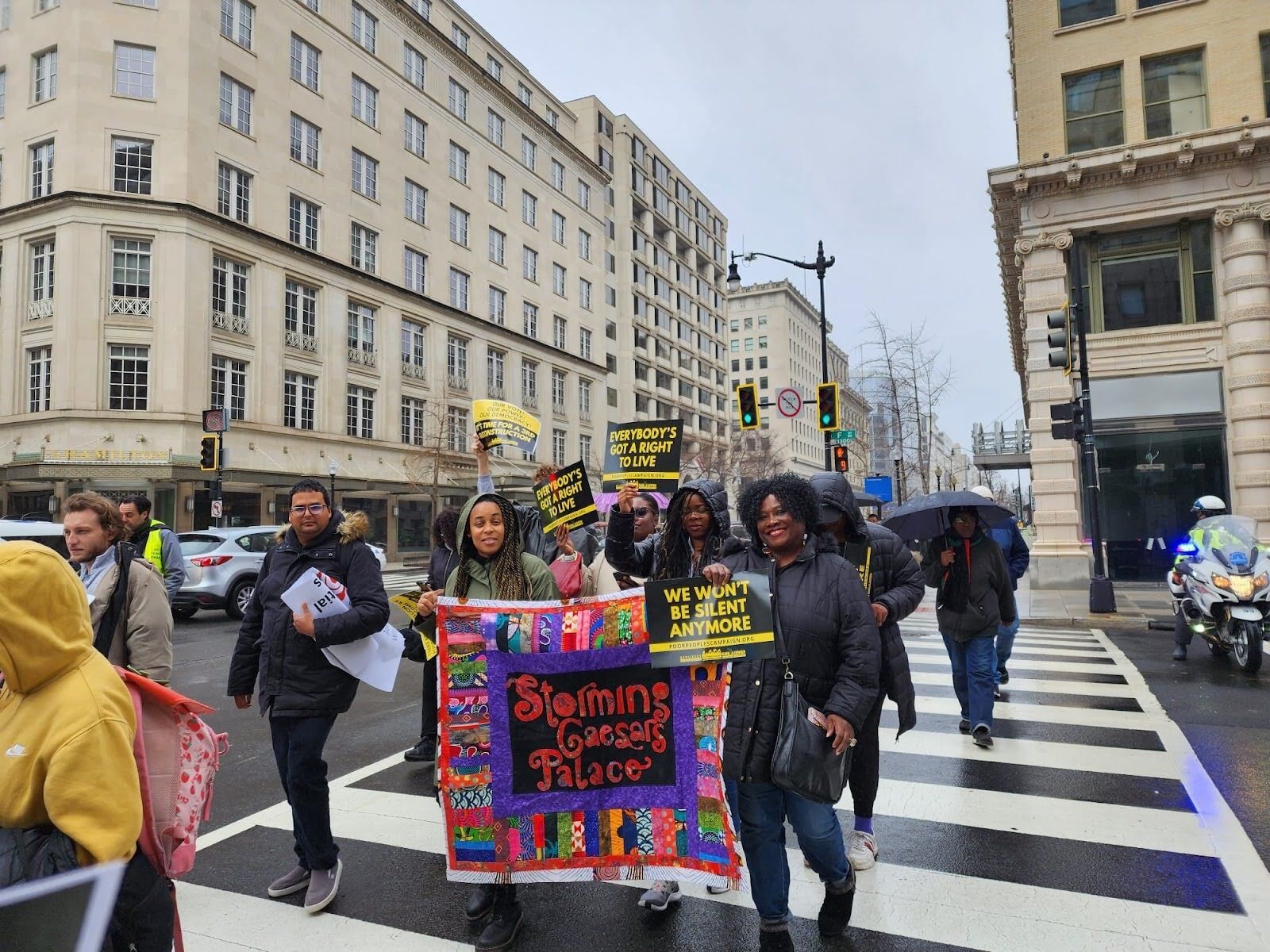 A group of people cross a street in downtown D.C., holding signs.