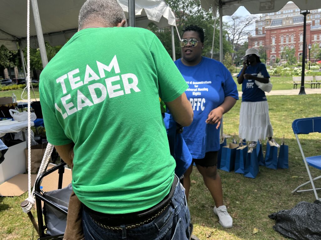 A man with a green shirt that reads "Team Leader" hands a shirt to an attendee. 