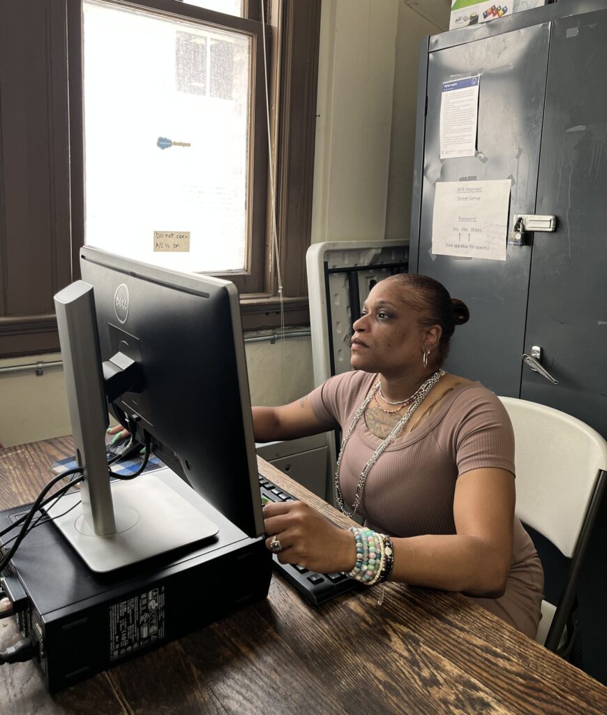 A Black woman in a brown dress sits at a computer, thinking