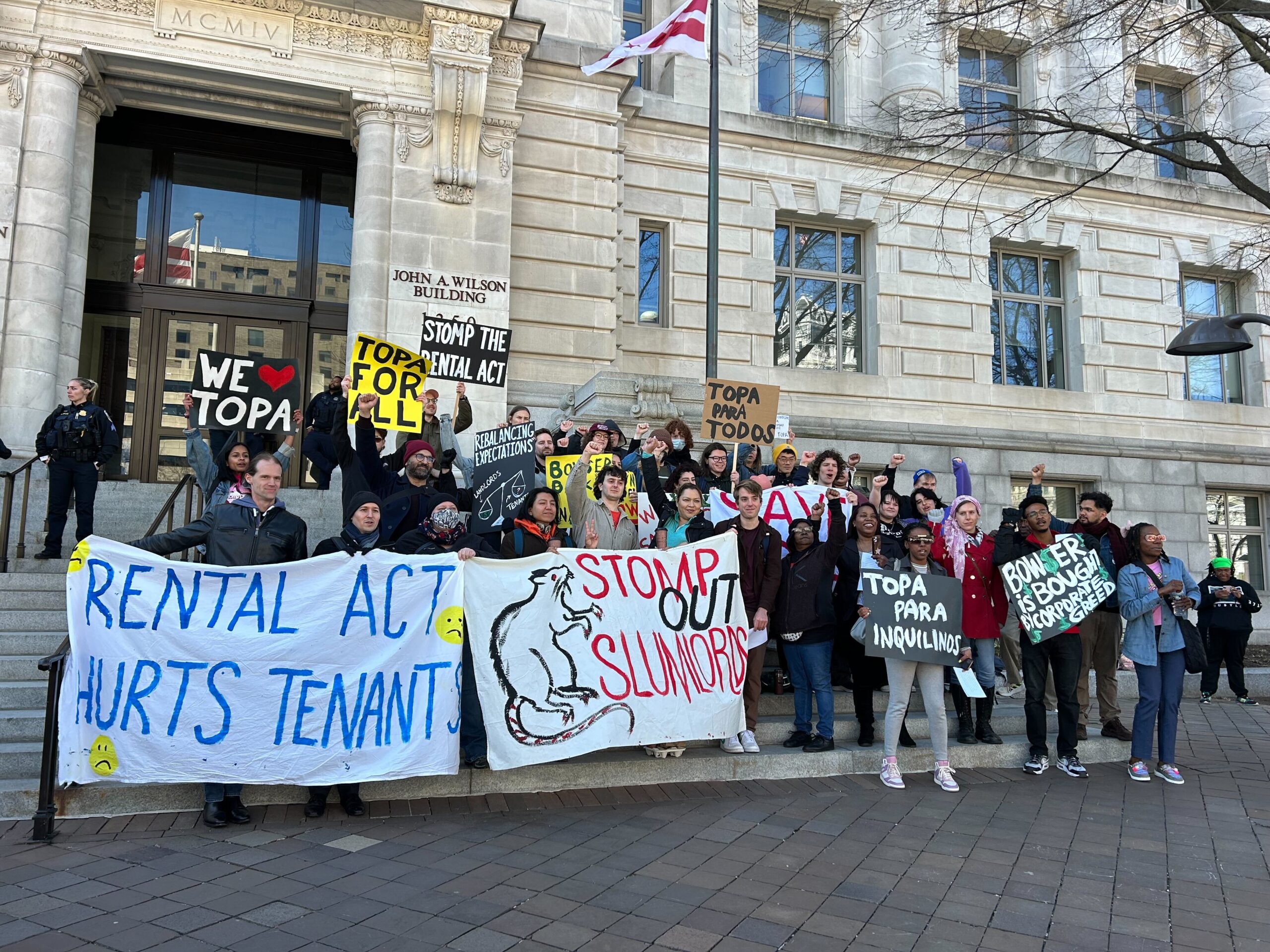 A group of people holding signs about tenants rights stand in front of a white marble building.