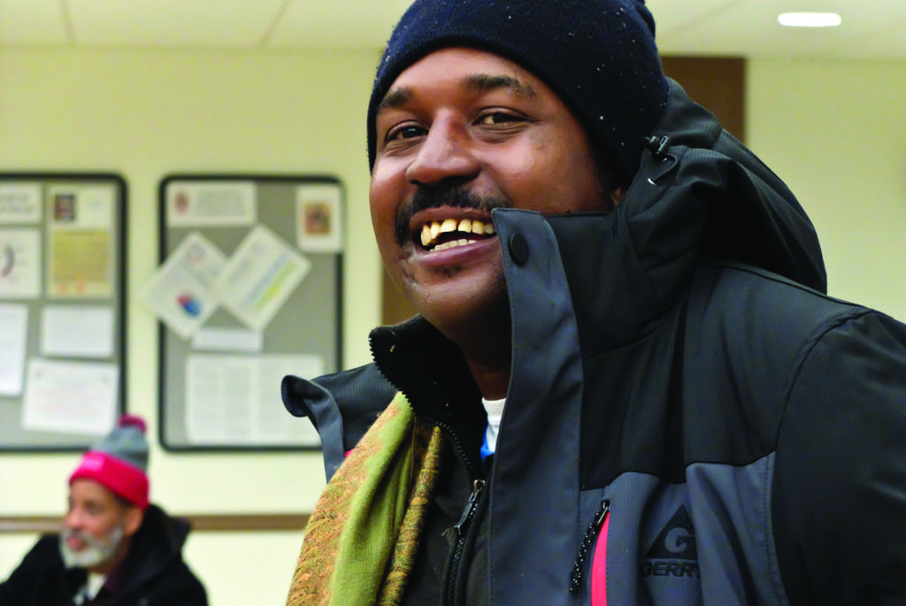 A Black man in a winter coat and hat smiles at the camera.