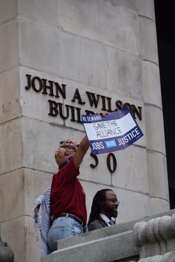 A woman holds up a sign reading "save the alliance" in front of D.C.'s city hall.