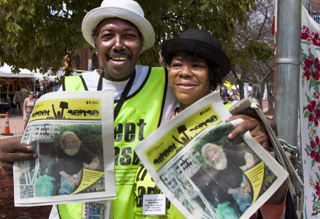 Two Street Sense vendors pose with their vests and newspapers.