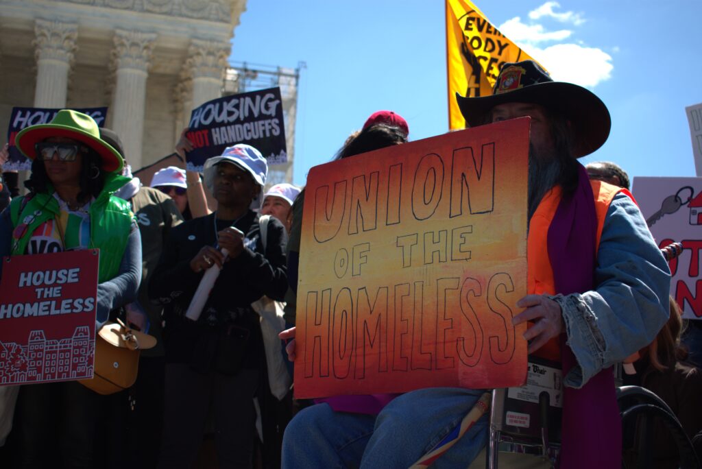 A man holds a yellow and orange sign reading "Union of the Homeless."