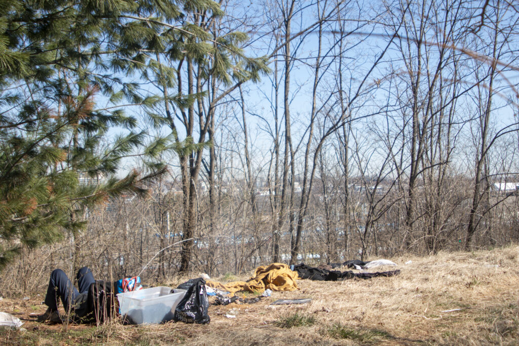 A man lays on dried grass outside his encampment on a hill overlooking the city.