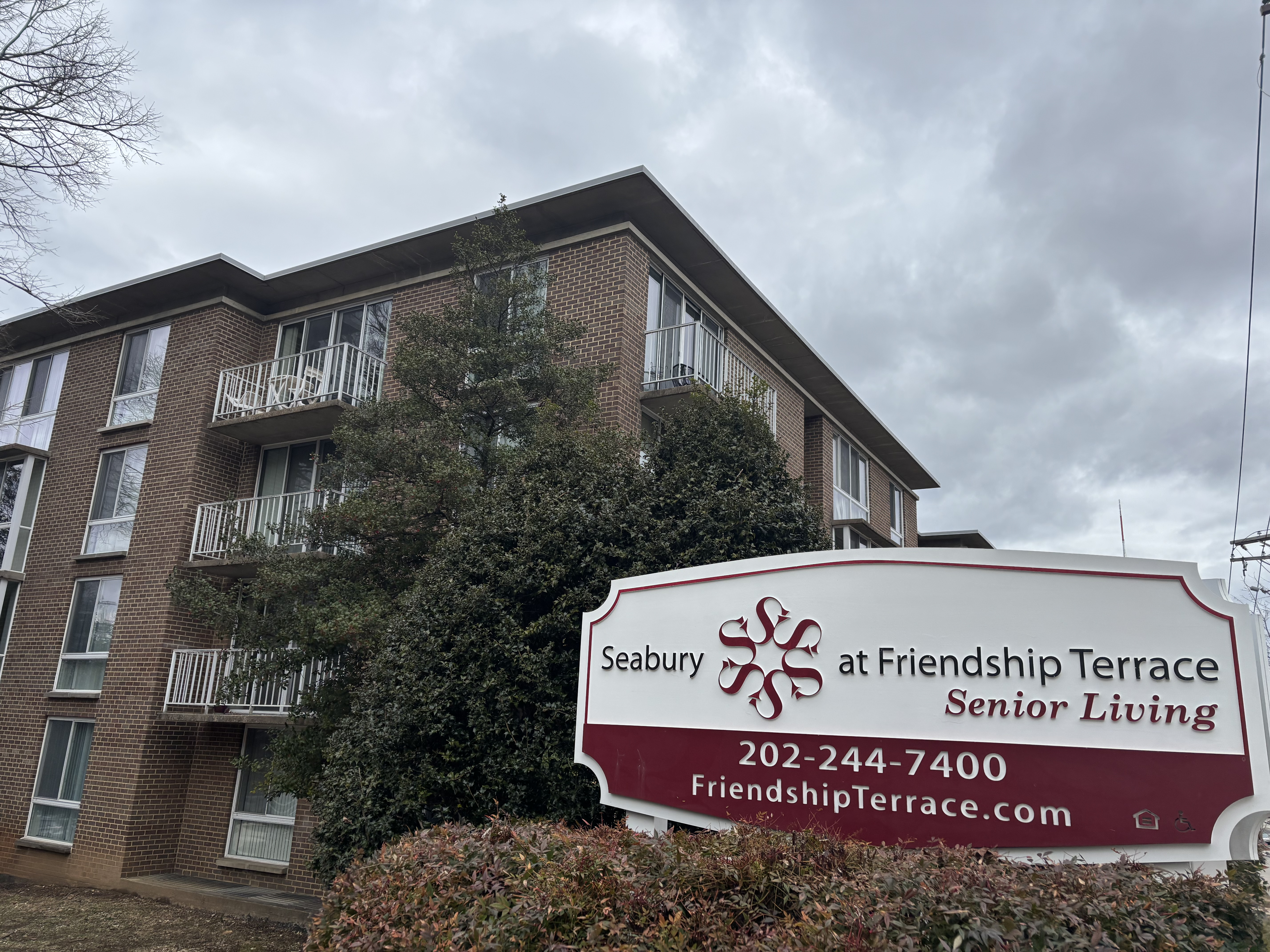 A brown apartment building with a red and white sign in front reading "Seabury at Friendship Terrace."
