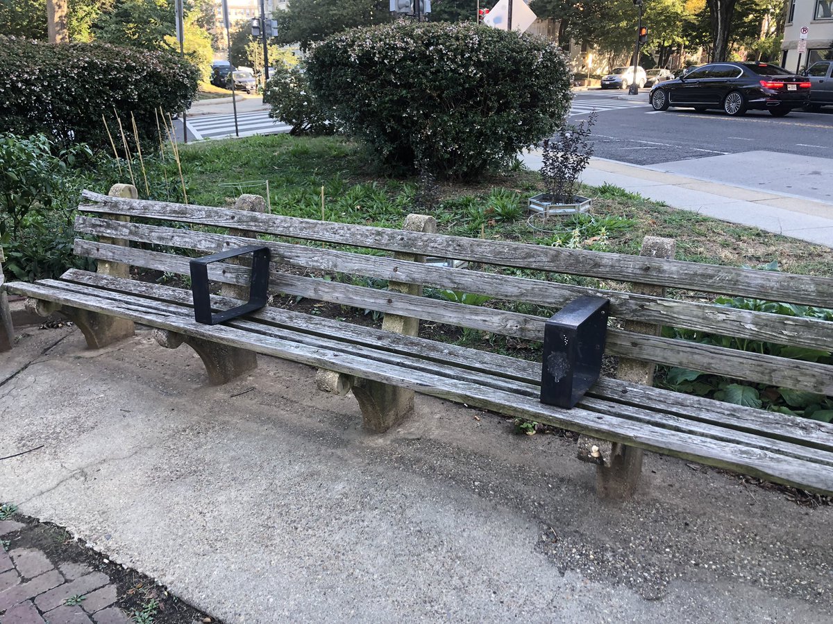A wooden bench with black armrests every few feet.