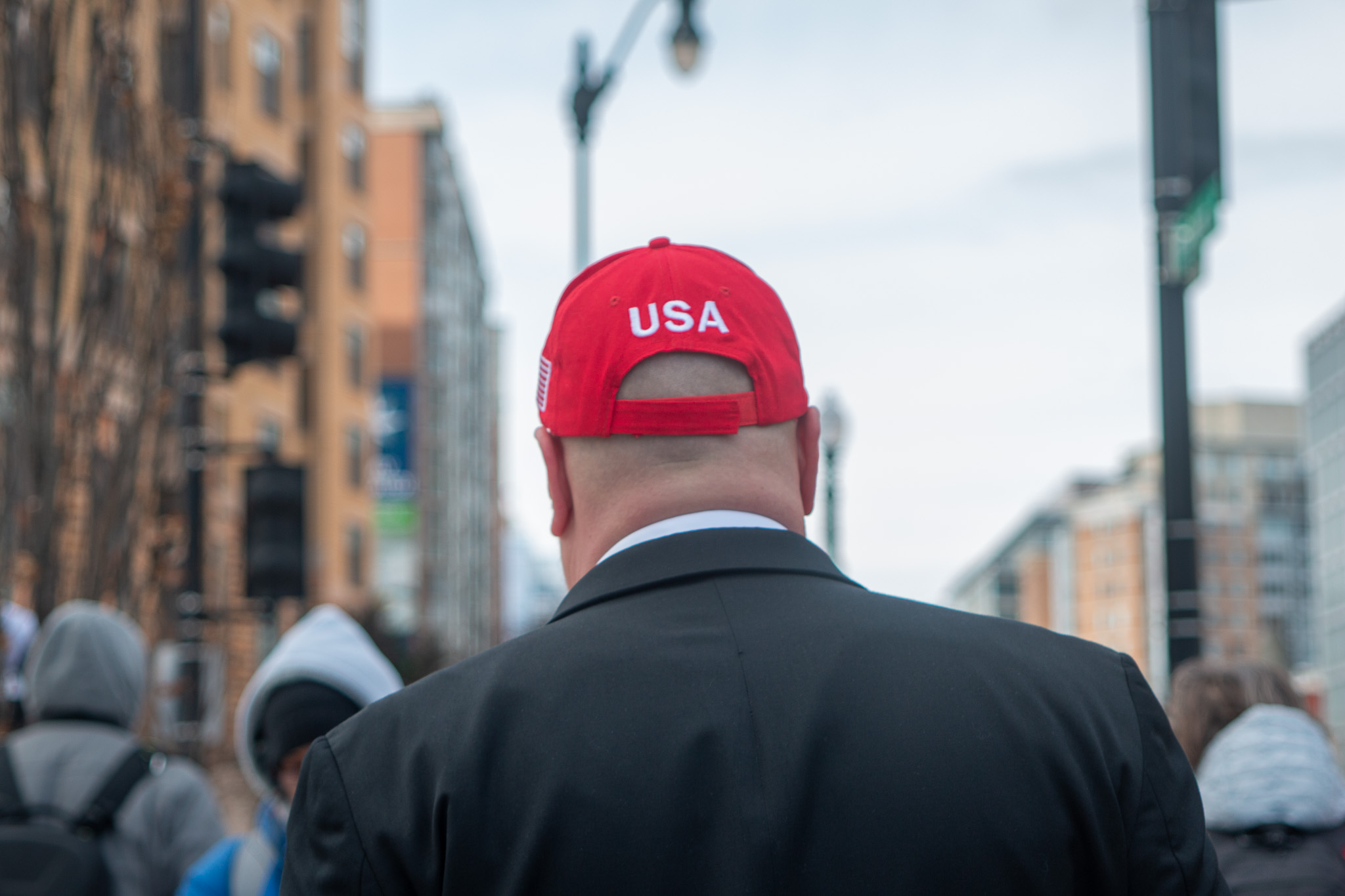A man in a red Trump hat that says USA stands facing away from the camera.
